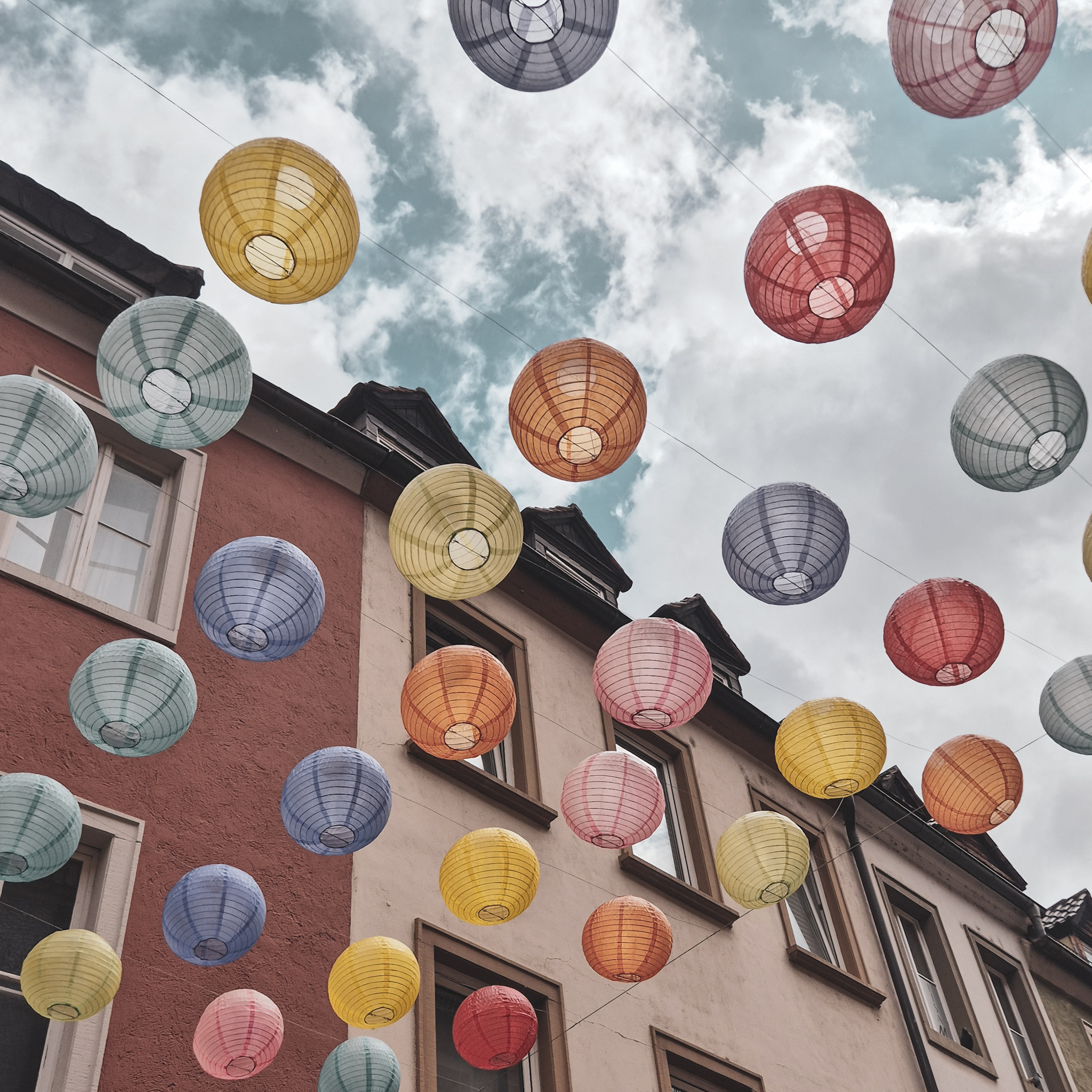 bunte Lampions, die zwischen Häusern in einer Gasse hängen. 