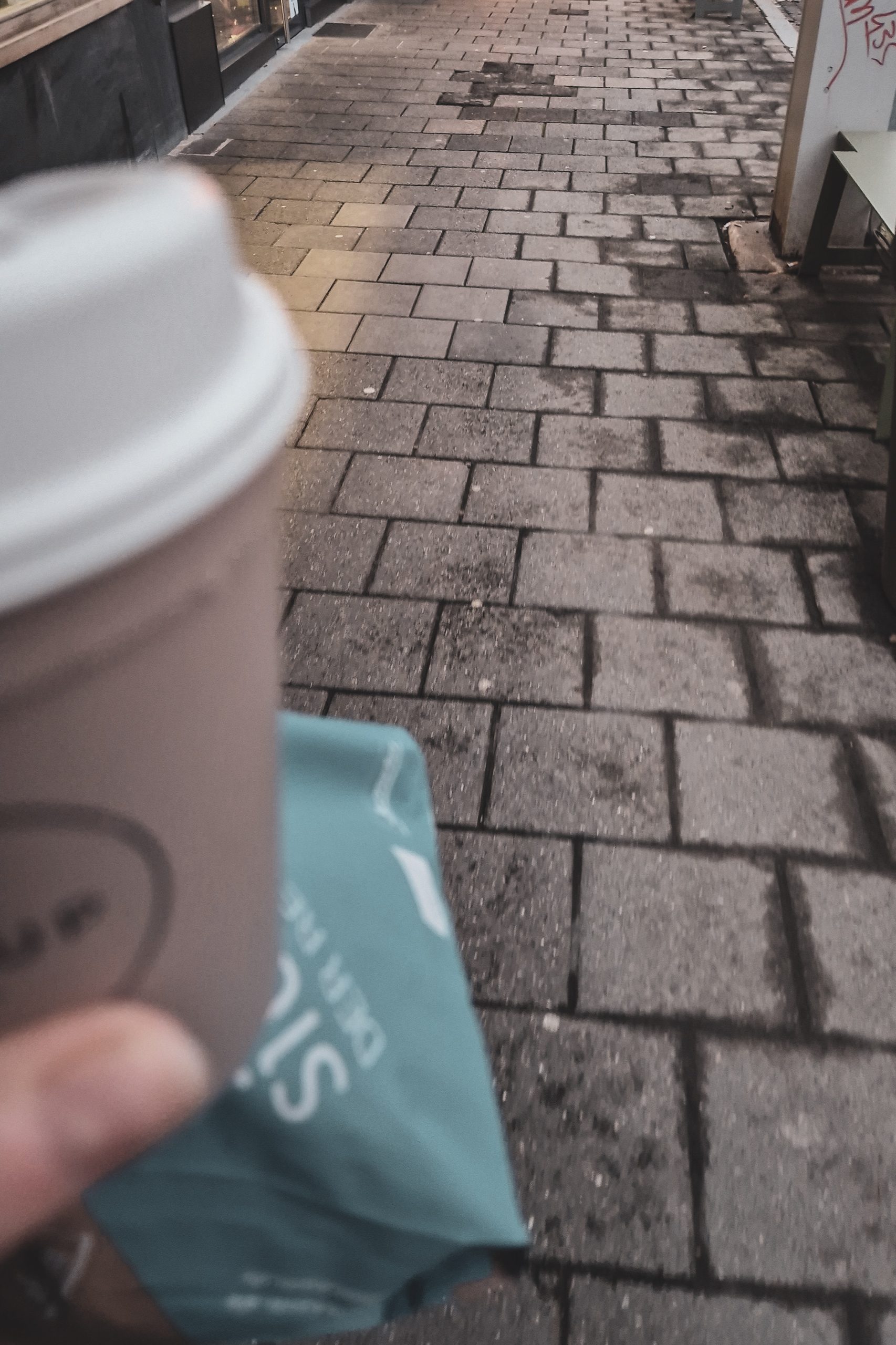 Kaffee und Tüte mit Frühstück in der Hand, Blick auf den Geweg.